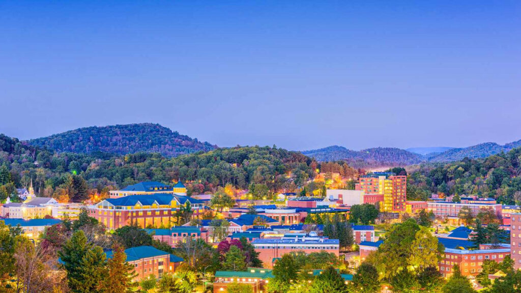 A small city with colorful buildings and treehouse cabins nestled among green, dusk-lit hills.