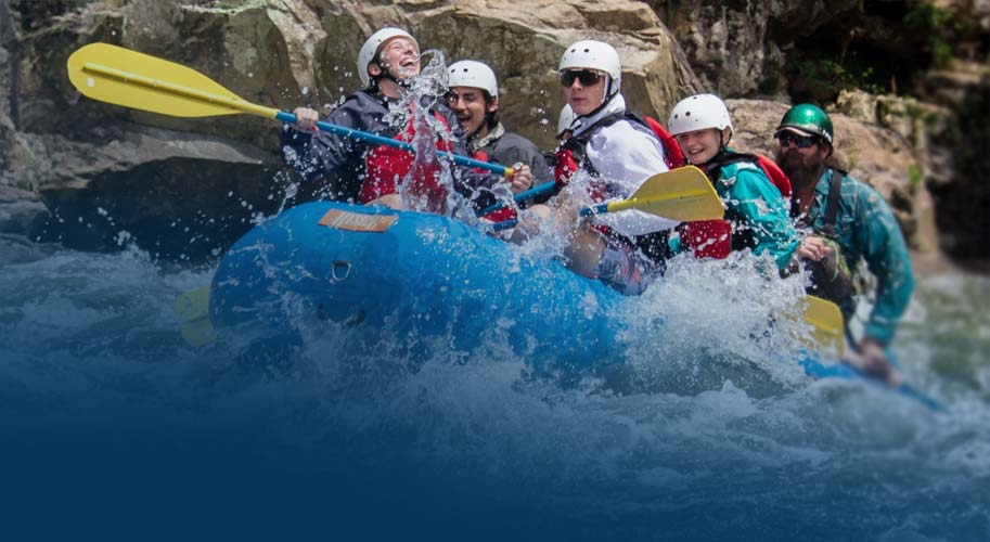 Five people with helmets whitewater rafting on a blue raft with Wahoo's Adventures.