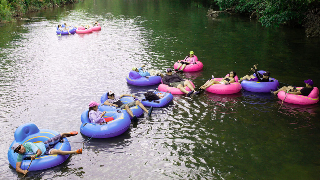 People relaxing on colorful tubes, floating past trees near Wahoo's Adventures Treehouse Cabin.