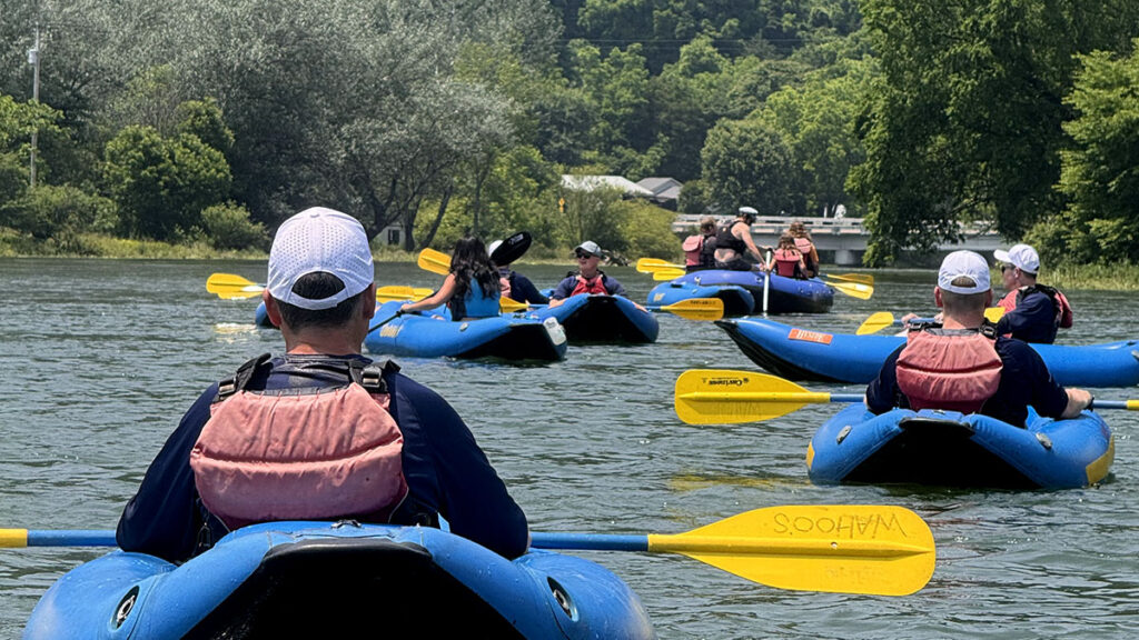 People kayaking in blue boats with yellow paddles, enjoying river rafting amid lush greenery.