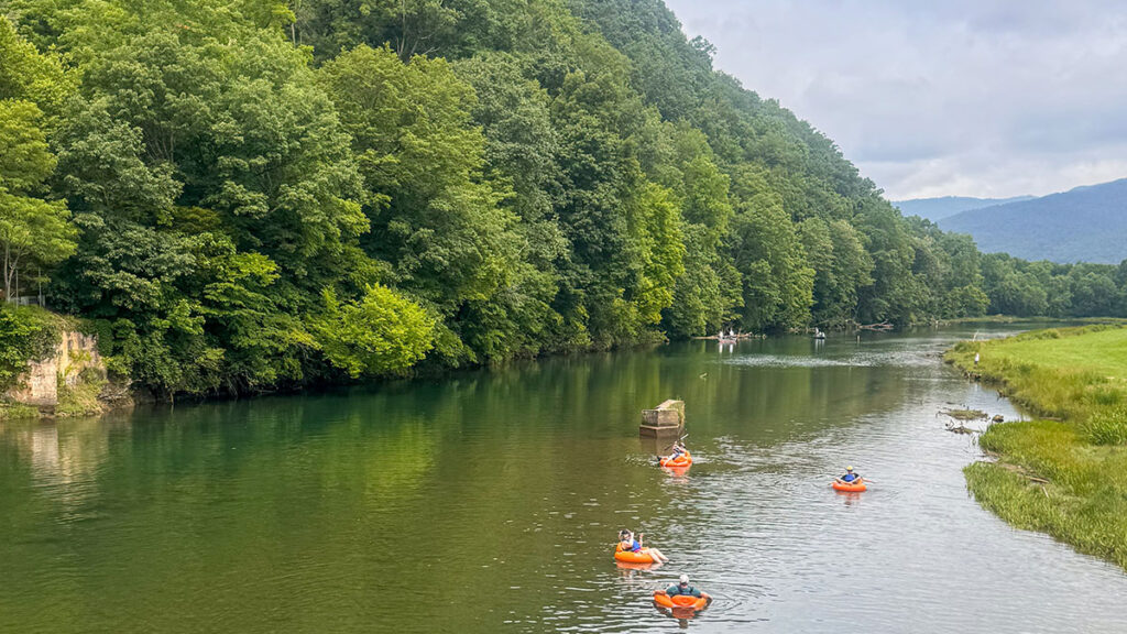 People in orange tubes float down a calm river with Wahoo's Adventures and lush green banks.