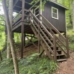 A small brown treehouse cabin on stilts with stairs, nestled in forest near Boone, NC.