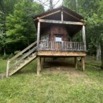 A small wooden cabin with a porch, like Treehouse Cabins Near Boone NC, amid trees and grass.