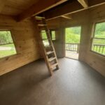 Interior of a wooden treehouse cabin near Boone NC with loft ladder, open door, and green views.