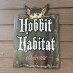 Sign reading Hobbit Habitat Welcome with hobbit ears, eyes, and Treehouse Cabins Near Boone NC.