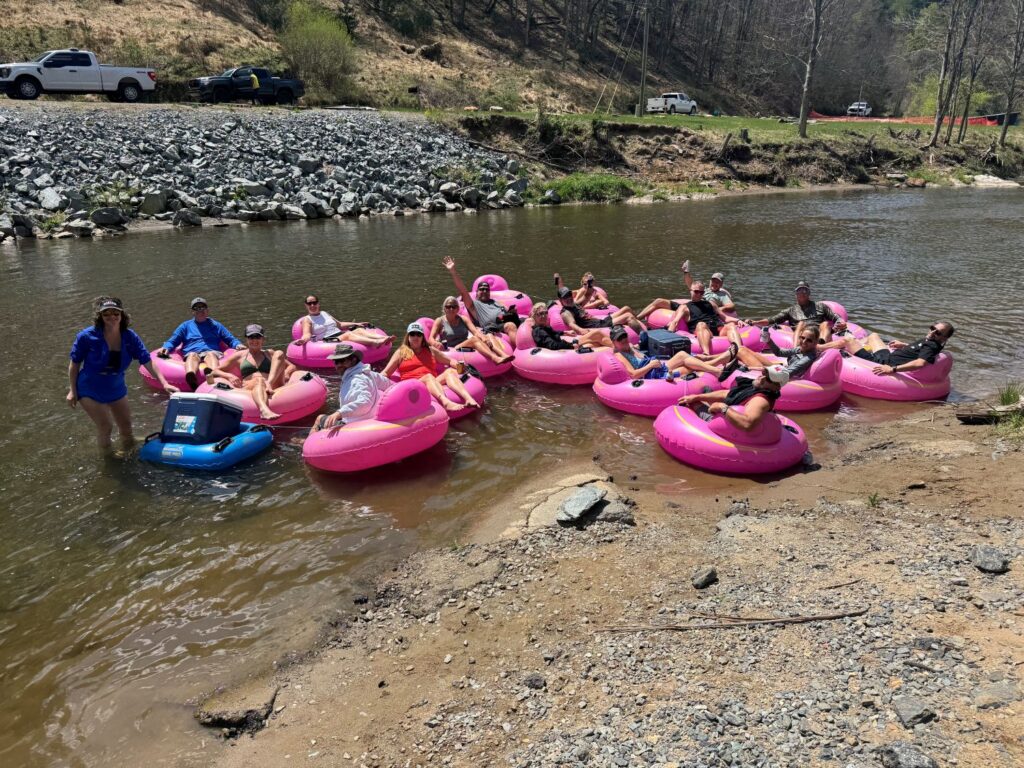 Group of people relaxing in pink tubes on a river near a rocky shore on a sunny day.