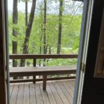 A wooden deck with a bench overlooks green trees at Treehouse Cabins Near Boone NC.