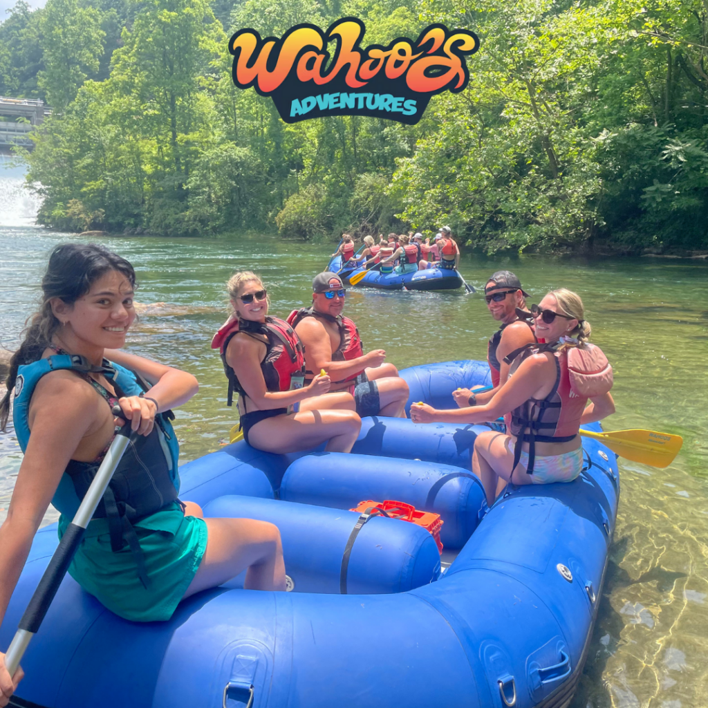 Five people in a blue raft on a river, smiling, with Wahoo’s Adventures logo above.