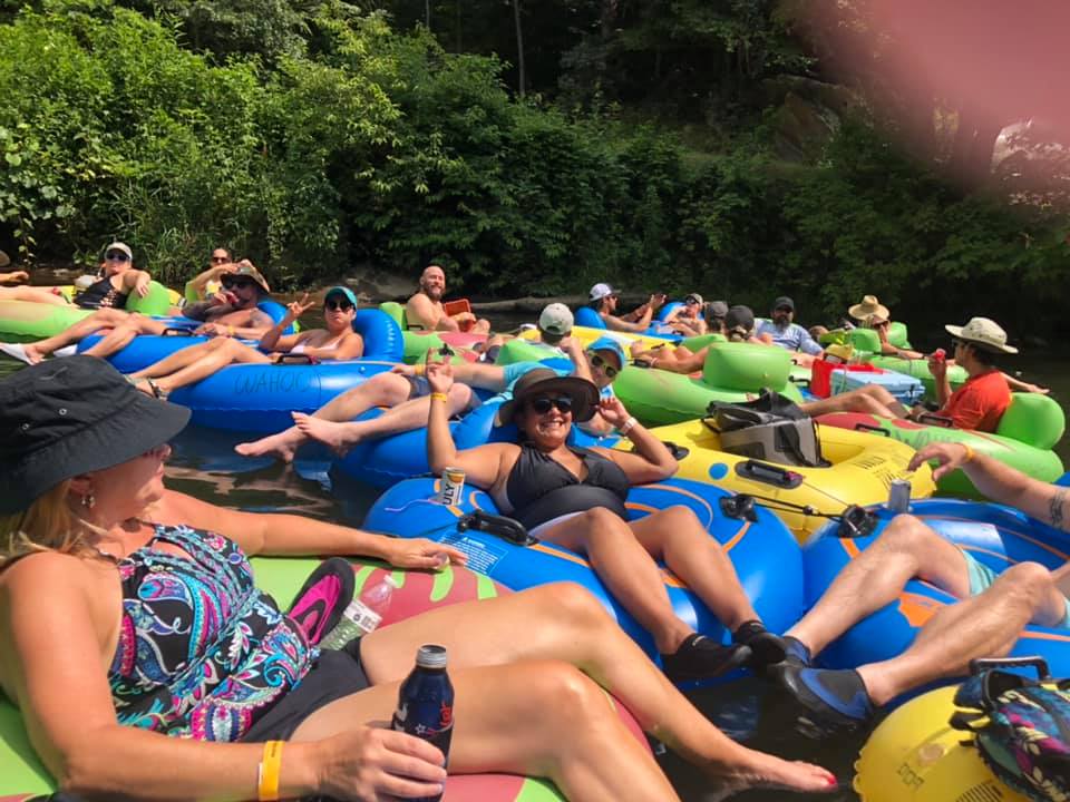 Group of people relaxing on colorful inflatable tubes in a river surrounded by greenery.